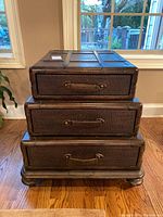 Front view of the stacked chest style coffee table showing three drawers and base on hardwood floor under window.