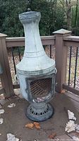 Front view of grey cast metal chiminea on pedestal showing grated front door and removable lid.