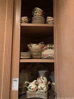 Overview of china set stacked in wooden cabinet, showing cups, saucers and plates.