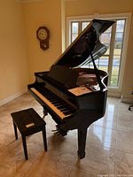 Angled view of polished black grand piano with open lid and matching bench.