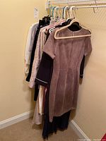 Photo of dresses and assorted ladies clothing hanging on a rack in a closet, including a taupe dress at front.