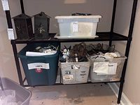Shelf with two black metal lanterns featuring snowflake cutouts on the top shelf, and three plastic totes with electrical cords, lights, and timers below.