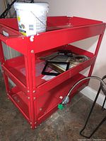Photo of red metal rolling cart with a white bucket on top and picture frames on middle shelf