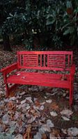 Front view of solid wood red bench with slatted back and seat, weathered and outdoors among dry leaves.