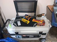Full view of wheeled cooler with folding seat and assorted grill and camping supplies placed on top.