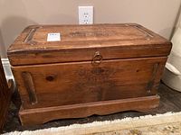 View of the chest front showing carved floral pattern on top and front panel, scratches, and natural wood grain.