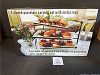 Box front shows the full assembled 3-tier porcelain serving set displayed with food and drinks.