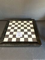 Top view of closed wooden folding chess board with visible chess squares and dark framed edge, shows wear and scratches.