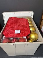 Plastic tote filled with gold ball ornaments, red tree skirt, and assorted baubles visible.