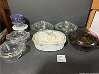 Full view of lot shows various covered casserole dishes and storage containers on grey background.