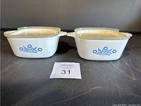 Two white vintage CorningWare 700ml casserole dishes with blue floral pattern, side by side with lids on.