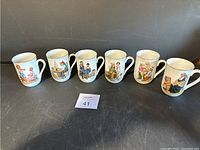 Six white ceramic cups with colorful Norman Rockwell inspired art, arranged in a line on a black surface.