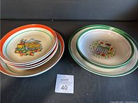 Seven ceramic pasta bowls stacked in two sets with different colorful hand-painted food and vegetable designs. Orange rim bowls with pasta pot illustration and green rim bowls with basket and utensils illustration.