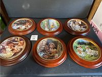 Six Sandra Kuck limited edition plates with wooden frames arranged on a black surface