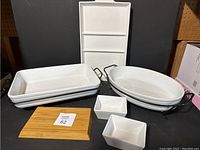 Front side view of all serving set items showing rectangular and oval ceramic dishes, small square bowls, and bamboo board