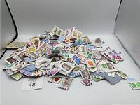 Large pile of mixed postage stamps mainly still attached to small cut pieces of envelopes or paper. Multiple colors and designs visible.