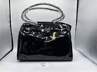 Front view of black patent leather purse with double handles and lock detail.