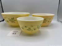 Front view showing the set of three yellow Pyrex mixing bowls with green floral trim