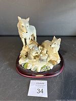 Figurine of four wolves posed on a snowy base with moss accents, mounted on a wooden platform with brass nameplate, viewed from the front.