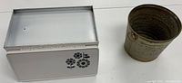 Side view of vintage metal bread holder with decorative flower design next to weathered tin can