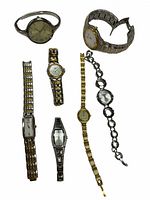 Top-down view of seven wristwatches including a variety of metal band styles and dial colors, laid flat on white background to show full lot