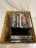 Top view of basket with 13 DVDs, showing titles including The Conjuring 2 (unopened), Mission Impossible, District 9, Lord of War, and others.