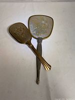 Hair brush and mirror laid flat showing gold colouring and floral embossed design on brush.
