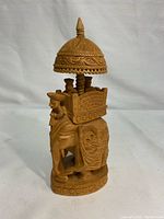 Front-left side view of the carved wooden elephant figurine showing detailed carvings and rider under an ornate canopy.