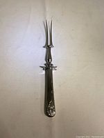 Full view of the stainless steel carving fork with decorative handle, showing the two-prong fork and floral embellishment on the handle.