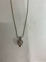 Silver chain necklace with cage pendant holding a pearl inside, centered on white fabric background.