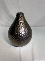 Front view of hammer-textured metal vase with bulbous shape and narrow opening.