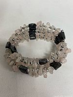 Magnetic wrap-around bracelet made of black hematite beads, light pink rose quartz chips, and small silver spacer beads, coiled in a circular form.