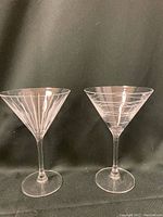 Two clear regular martini glasses with etched linear and swirl designs on bowls, slender stems, and flat bases.