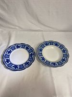 Two decorative ceramic plates shown side-by-side with scalloped edges and blue floral patterns on white background.