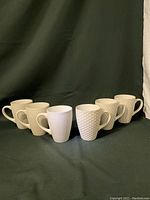 Set of six white Mikasa stoneware mugs arranged in a row, showing different raised textures and embossed patterns on each mug.