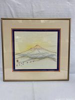Front view of framed mountain landscape sketch with beige and blue matting inside gold-colored frame.