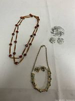 All jewelry items displayed together on white fabric, showing three sets of vintage costume jewelry