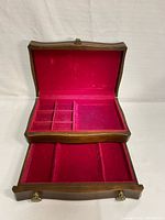 Open jewelry box showing red velvet interior with compartments and a lower drawer.