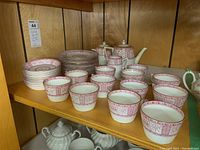 Full view of vintage Brixton china tea set pieces arranged on shelf showing cups, saucers, plates, creamer, sugar bowl, and teapot with pink trim pattern.