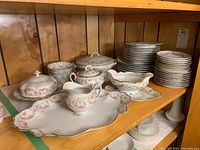 Full set displayed on wooden shelf including stacks of plates, covered serving dishes, sugar bowl, creamer, and large serving platter.