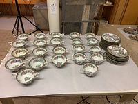 Overall view of 22 bone china consommé bowls in two handle styles and matching saucers arranged on table
