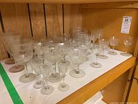 Over 30 pieces of vintage clear crystal stemware and dessert bowls with etched floral and geometric patterns on wooden shelves.