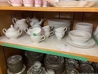 Shelved white ironstone dishes with fluted design including stacked plates, cups, teapot, creamer, sugar bowl.