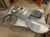 Overview of six metal serving trays and platters of various shapes and decorative textures laid out on a white surface.