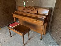 Front view of Henry Herbert Mason & Risch upright piano, showing wooden music rack and tapered legs with brass casters, alongside matching wooden bench with red piano book on top.