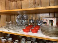 Shelf with clear glass Pyrex baking pans including rectangular and pie plates, red crab-shaped ceramic covered dishes, and metal lobster serving trays.