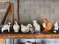 Full view of all 7 farm animal figurines and decor displayed on a wooden shelf against a concrete block wall, showing a variety of materials including wood and ceramic.