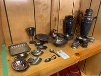 Full view of all items on wooden shelf: two cocktail shakers, goblet, shell dishes, small bowls and utensils