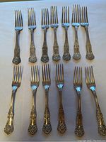 Seven dinner forks (top row) and six salad forks (bottom row) laid out on white background