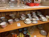 Shelf with a collection of assorted bone china tea cups and saucers, including multiple floral patterned pieces and small dishes.